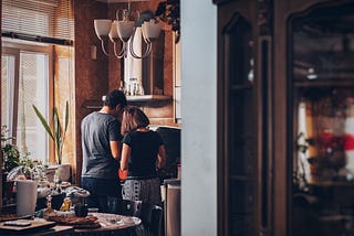 A couple stand in a kitchen in front of a stove cooking together with backs to the camera