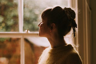 A beautiful woman standing in front of a window, in warm morning sunlight, holding a cup of tea.