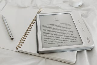 A white cased ereder on a open white notebook with a good spiral binding. There is a silver pen to the left. All are on a white cloth.