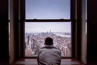 A man in a grey hoodie looking from his window in the distance on New York city in America