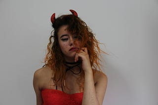 A woman with horns and a red dress with a sour face.