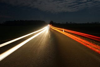 a time-lapse photo looking down a highway and showing the red lines of taillights on one side and the white lines of headlights on the other.