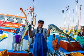 A smiling woman holds two large fish in each hand.
