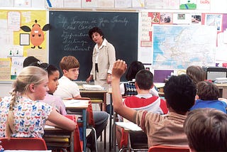 A typical classroom where a teacher stands in front of students delivering educational content.