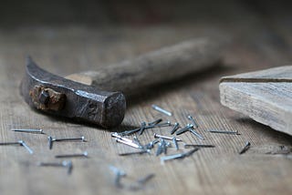 A builder’s hammer and nails laid down on a table. Because writing is building.