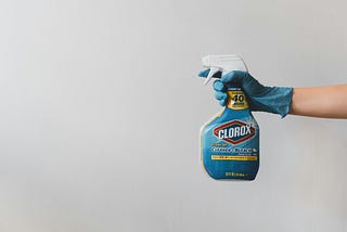 A gloved hand holding a spray bottle of Clorox.