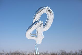 two silver mylar balloons, one in the shape of the number four, the other a zero, floating with the sky in the background