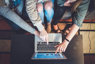 Three people sitting in front of the laptop and pointing fingers at the screen showing things to each other