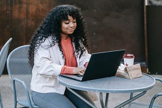 A black female writer typing on a laptop with coffee on table