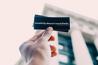 A hand holding a small card with the words 'Creativity doesn't need limits' on it