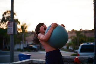 young kid wrestling up a yoga ball in the gym