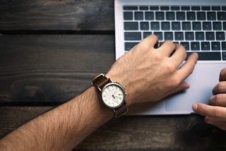 man looking at watch typing on laptop