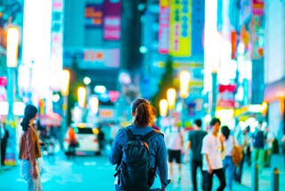 Woman with backpack walking down blurred, colorful street in Asia.