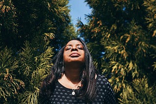 A Black woman in nature with her eyes closed and a peaceful look on her face.