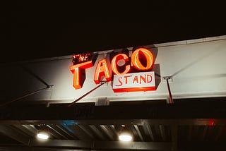 An orange neon sign reading “The Taco Stand.”
