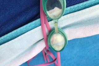 Sea green goggles with a hot pink strap on a blue and white striped towel