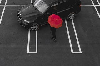 A black SUV in an empty parking lot with a person holding a red umbrella next to it.