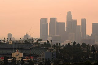 A view of downtown L.A over the shoulder of Dodger Stadium, on a hazy with a peachy orange sky.