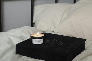 White bed and a book and candle on top of it.
