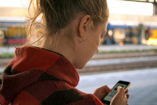 Photo of a woman reading a text message. She’s wearing a red jacket.