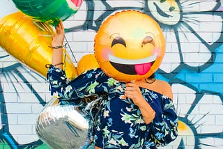 A woman holding a smiley face balloon in front of her own face