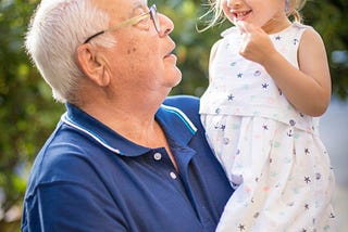 A grandpa holds his granddaughter in his arms.