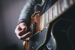 Closeup of a man strumming a sunburst-colored electric guitar