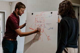 A person draws on a board and another person watches.