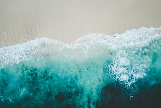 Gods-eye view of rich, blue waves crashing down onto a nearly empty beach.