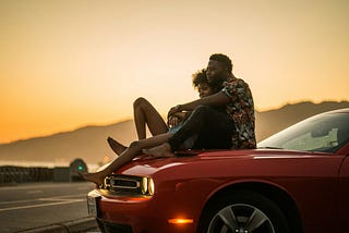 Couple hugging on the hood of a red car.