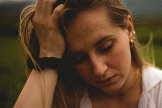 A worried woman runs her hand through her hair, eyes cast down. solemn face