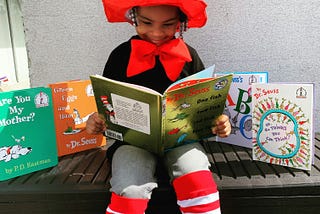A child reading a Dr. Seuss book surrounded by his most popular titles.