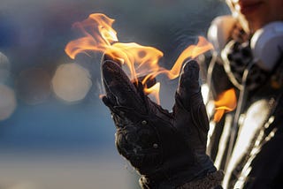 A person’s gloved hand with a flame on the palm and fingertips