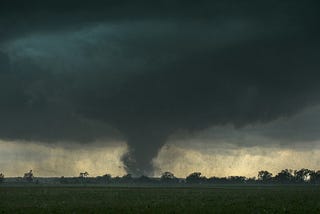 Tornado in distance along a treeline with ominous clouds overhead