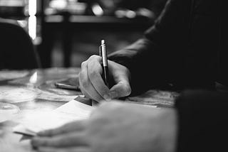 Black-and-white image of a hand writing on a notepad.