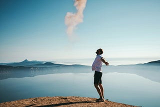 A happy man opens his arms wide against a scenic backdrop of sky and lake