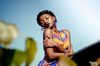 A beautiful woman wearing a vibrant colored dress of yellow, red, and purple, with her arms wrapped around herself in self-love.