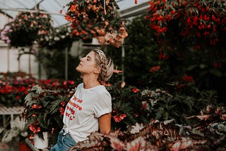 Woman standing in a greenhouse full of plants, eyes closed as if she is meditating