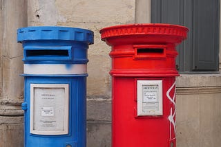 Blue post, red post side by side near a wall for people sending letters.