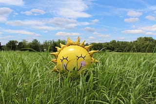 Sun balloon with a smiling face sitting on a field of green grass.