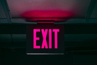 Neon pink “EXIT” sign illuminated against a dark ceiling