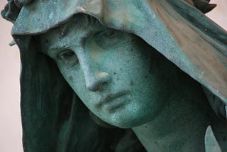 A stone statue of a troubled face under a hood.