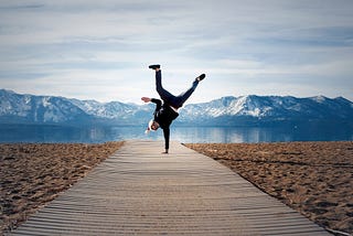 A man doing a one-handed handstand with mountains behind him