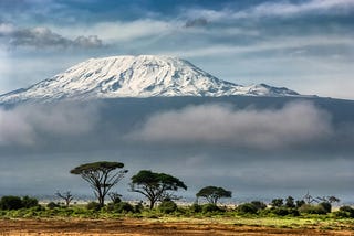 Snow-capped Mount Kilimanjaro, rises above a Tanzanian grasslands at its base.