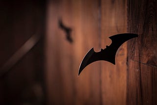 A Batman batarang stuck inside a wooden wall.