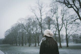 Photo of the back of a woman walking as snow is falling