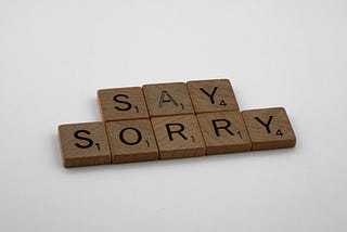 Wooden scrabble tiles spelling “Say Sorry”