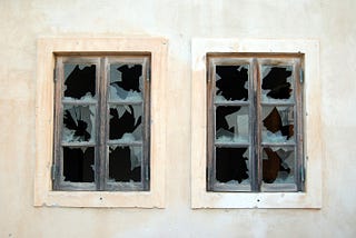 Two windows, 6 panes each with all glass broken out on a stucco building.