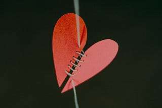 A severed paper heart being sown together.