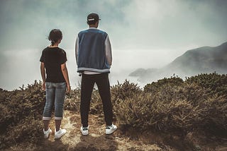 man and woman looking over cliff into mist